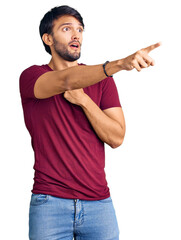 Handsome hispanic man wearing casual clothes pointing with finger surprised ahead, open mouth amazed expression, something on the front