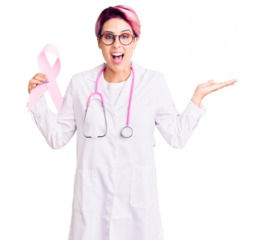 Young beautiful woman with pink hair wearing doctor stethoscope holding cancer ribbon celebrating victory with happy smile and winner expression with raised hands