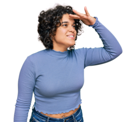 Young hispanic woman with curly hair wearing casual clothes very happy and smiling looking far away with hand over head. searching concept.