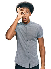 African american man with afro hair wearing casual clothes doing ok gesture shocked with surprised face, eye looking through fingers. unbelieving expression.