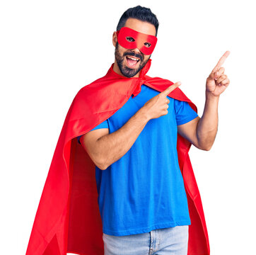 Young hispanic man wearing super hero costume smiling and looking at the camera pointing with two hands and fingers to the side.