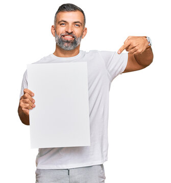 Middle age handsome man holding blank empty banner pointing finger to one self smiling happy and proud
