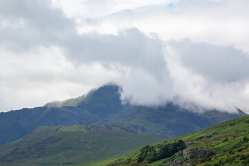 View of Crib Goch from the Llynnau Mymbyr lake by the small small town of Capel Curig on a cloudy day, Image shows a beautiful scenic view of the mountains of Snowdonia with cloud covering the sumit