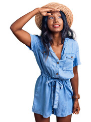 Young indian girl wearing summer hat very happy and smiling looking far away with hand over head. searching concept.