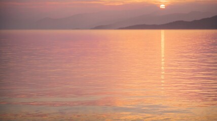 Naklejka premium A breathtaking sunset scene over a calm sea, with the warm hues of orange, pink, and purple painting the sky and reflecting on the water. The silhouettes of distant mountains.