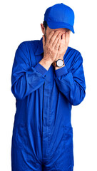 Middle age handsome man wearing mechanic uniform with sad expression covering face with hands while crying. depression concept.