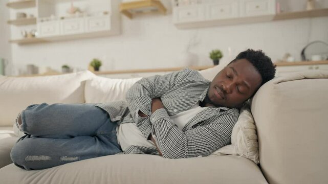 African American man sleeping on sofa in living room of apartment, relax time. Exhausted young male person lying on couch and dozing off, tiredness after working day, afternoon nap and relaxation