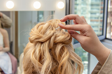 Naklejka premium Female stylist styles the hair of blonde woman. Styling hairstyles for wedding or event. Invisible hairpin closeup