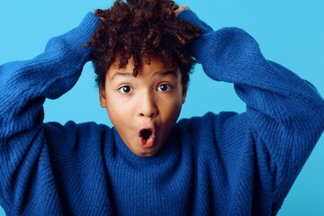 Young african american woman displays shock and surprise with hands on head against a neutral...