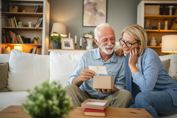 Senior husband read greeting card from a gift with his mature wife