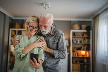 Senior couple use mobile phone together at home