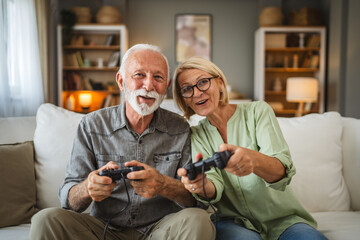 Senior couple sit on sofa and play video games on joystick at home