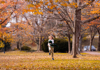 Fototapeta premium Funny kid running near autumn tree in the autumn park. Active child run and jump in autumn park outdoors. Little kid running near park. Autumn season.