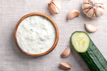Fresh tzatziki in a wooden bowl on linen fabric. Refreshing dip, soup or sauce, made of salted strained yogurt, mixed with cucumbers, garlic, salt, olive oil, lemon juice and herbs, served cold. Photo