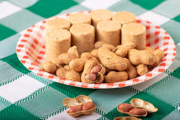 Peanuts, portion of peanuts in shell and paçoquinha (peanut candy) on a plate, on a green and white checkered tablecloth. Selective focus.