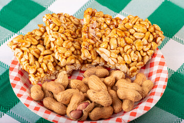 Peanuts, portion of shelled peanuts and pé-de-moleque (peanut candy) on a plate, on a green and white checkered tablecloth. Selective focus.
