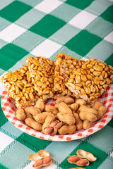 Peanuts, portion of shelled peanuts and pé-de-moleque (peanut candy) on a plate, on a green and white checkered tablecloth. Selective focus.