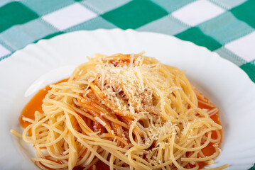 Pasta, portion of spaghetti noodles with grated cheese on a white plate on a green and white checkered tablecloth. Selective focus.