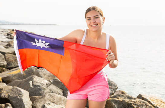 Enjoying vacation in Taiwan. Young woman with national Taiwanese flag on the seashore on a sunny day - Powered by Adobe