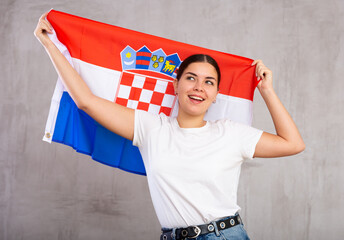 Joyful smiling young woman waving state flag of Croatia against gray wall background