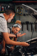 Male and female auto mechanics examining at discussing problem with car