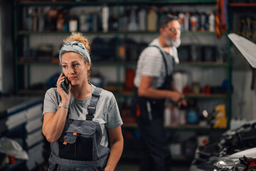 Female worker having phone conversation with customer at car repair shop