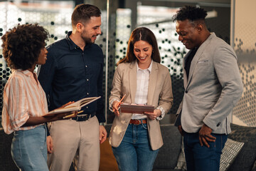 Interracial casual businesspeople standing at office with paperwork.
