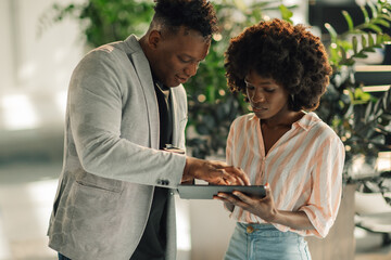Diverse businesspeople scrolling on tablet at green corporate office.