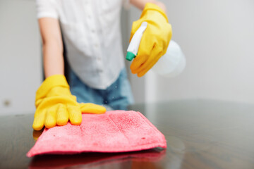 Woman in yellow gloves cleaning table with rag and solution bottle