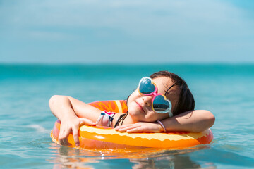 Little Asian child girl in swimwear and sunglasses with swim ring playing in the sea in summer sunny day. Happy children kid enjoy and fun outdoor lifestyle travel ocean on beach holiday vacation. © CandyRetriever 