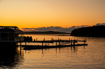 Sunset Over a Dock in Bar Harbor Maine. A calm, golden sunset casts long shadows across a wooden dock in Maine. The water is still and reflects the warm colors of the sky. A small building is silhoue