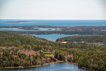 Aerial View of Islands and Ocean in Maine. A view of a small island with a house on it, surrounded by water and forested hills. The island is in the foreground, with the ocean and several other small