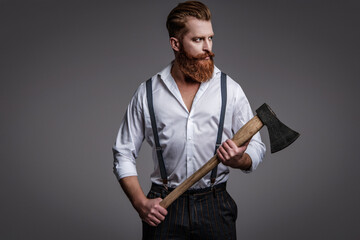 Brutal mature bearded man with redhead beard and moustache in retro suspenders hold axe isolated on...