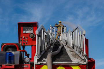 Firefighter on ladder, spraying water on fire, side view
