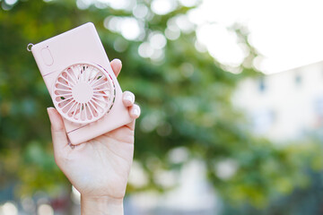 Unrecognised Woman Holding  Handheld Fan In Hand On Garden Background. Portable Fan. Summer Device. Climatic Change. Small Ventilator © Karyna