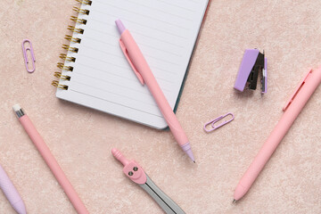 Pens with notebook and different school stationery on beige grunge background