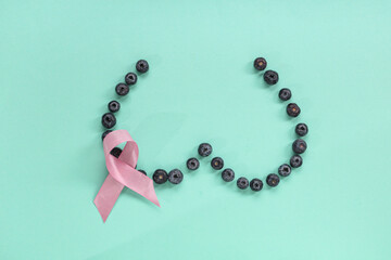Female breast made of blueberry and pink ribbon on color background. Cancer awareness concept