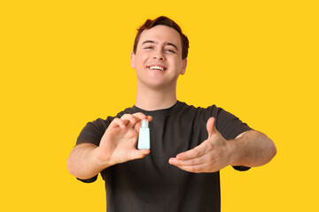 Young man with sanitizer on yellow background