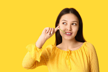 Beautiful young Asian woman with chewing gum on yellow background