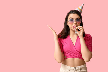Beautiful young woman in party hat with whistle on pink background
