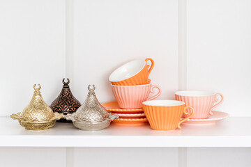 Decorative coffee cups and containers in various shades of orange, arranged neatly on a white shelf.