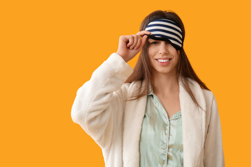 Young woman in pajamas and mask on yellow background