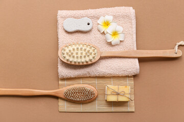 Massage body brushes, bamboo rug, towel, plumeria flowers, pumice stone and soap bars on brown background, closeup