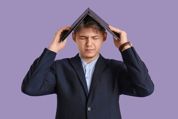 Young businessman with journal suffering from headache on lilac background