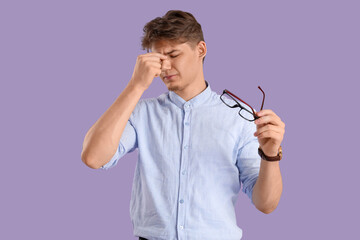 Young businessman suffering from headache on lilac background
