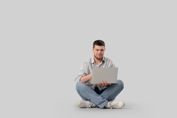 Young bearded man using laptop on light background