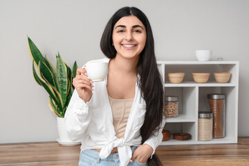 Beautiful young happy woman with cup of tea in kitchen at home