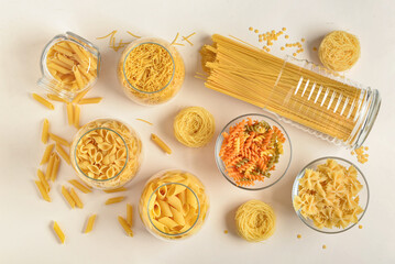 Composition with different uncooked pasta in glass bowls on light background