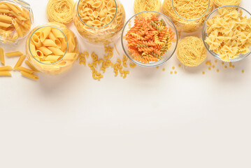 Composition with different uncooked pasta in glass bowls on light background