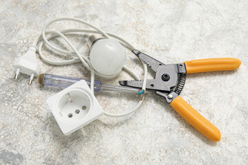 Electrician's tools, socket and light bulb on white grunge background